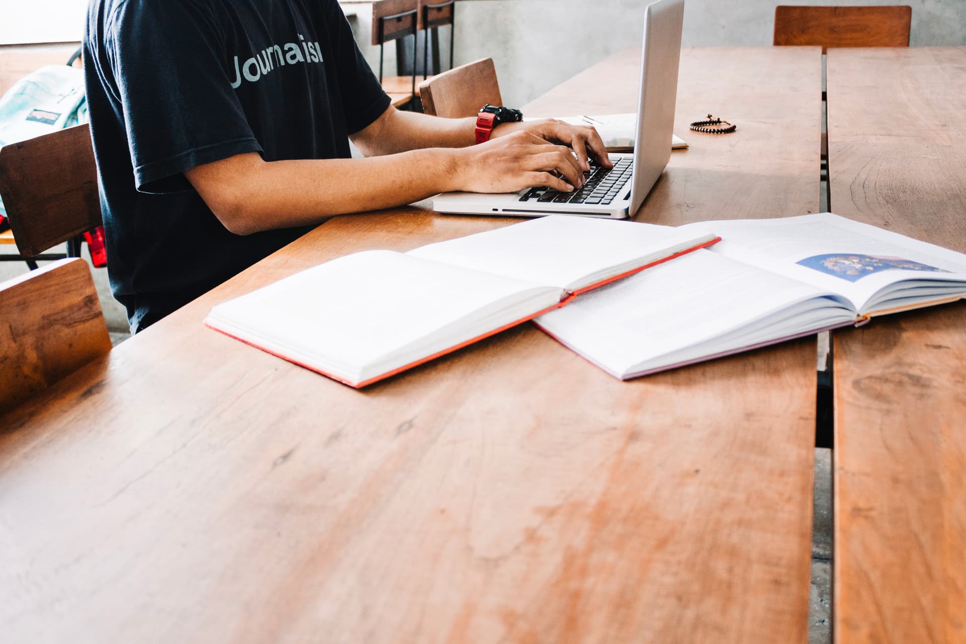 Person writing at desk with laptop and papers